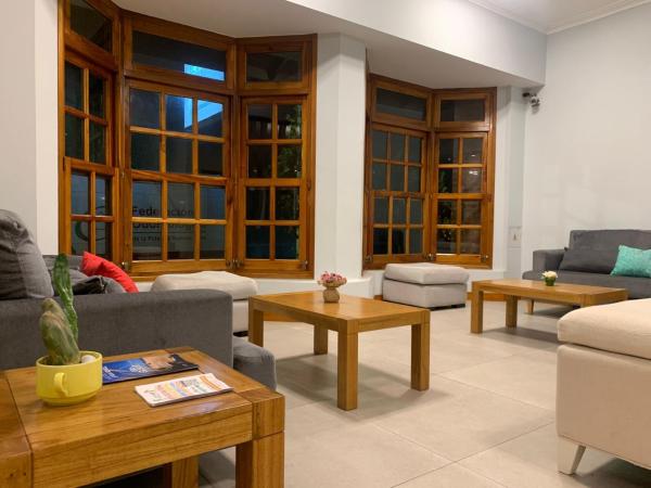 una sala de estar con sofás, mesas y ventanas en De La Plaza Hotel en Villa Gesell