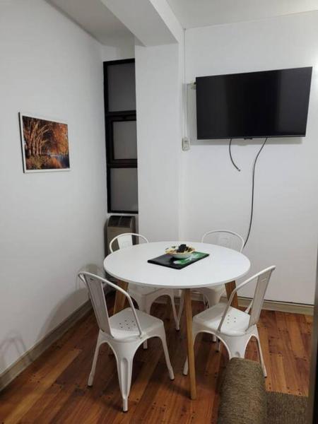 mesa blanca con sillas y TV en la pared en Departamento Plaza España con cochera en Mendoza