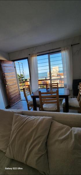 sala de estar con mesa, sillas y ventanas en Duplex premium Punta mogotes waikiki en Mar del Plata