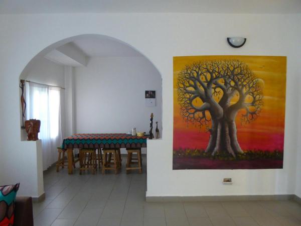 Interior of Sarawally Guesthouse with white walls, tiled floor, wooden stools, and colorful baobab tree painting
