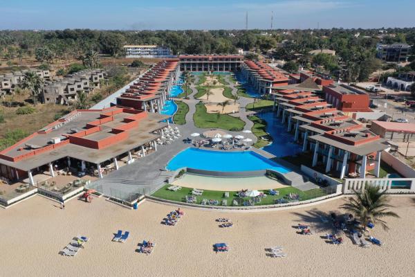 aerial view of a beachfront hotel with two wings, swimming pools, sun loungers on sand and green lawns