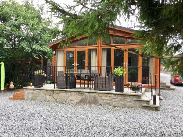 Wooden lodge with large glass doors and windows, outdoor seating on stone patio, surrounded by trees
