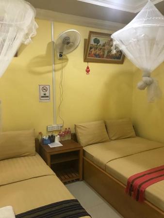 Simple guesthouse room with double bed, mosquito net, small wooden nightstand, wall fan, and no smoking sign