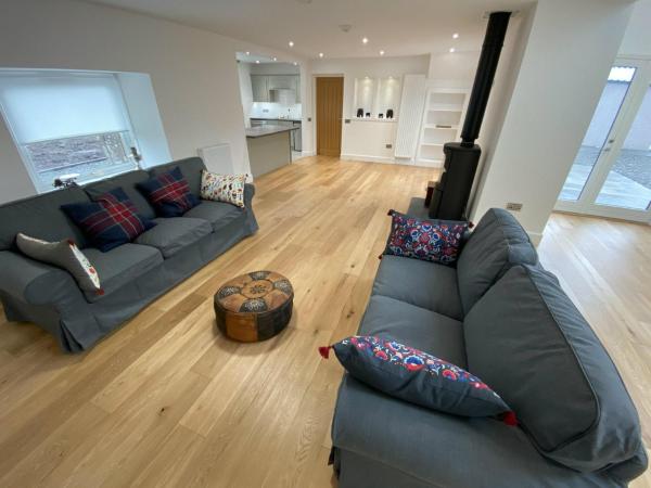 Living room with two grey sofas, patterned cushions, wooden floor, wood-burning stove, and open kitchen area
