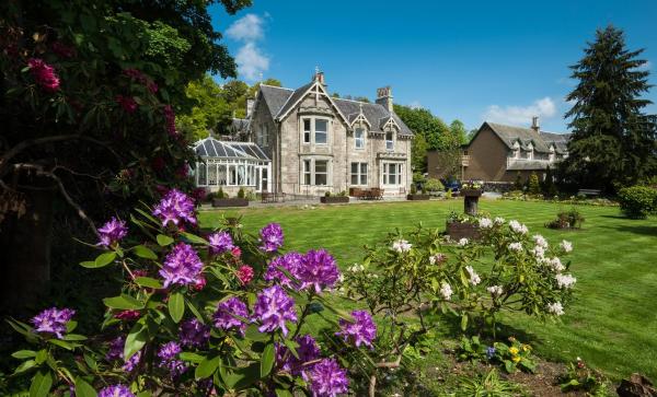 Stone guest house with conservatory and large lawn garden with purple and white flowers under blue sky