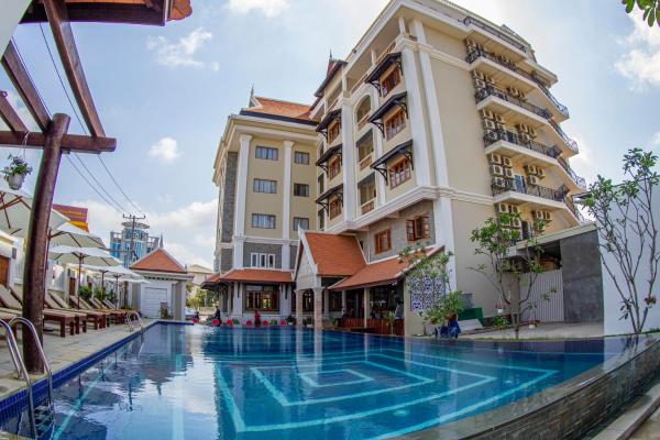 Outdoor swimming pool beside a multi-story hotel building with balconies and lounge chairs under umbrellas