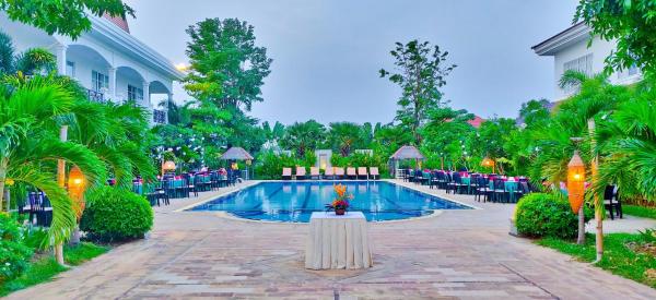 Outdoor swimming pool surrounded by palm trees and tables with chairs at Glorious Hotel