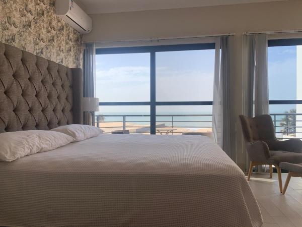 bed with tufted headboard and pillows facing large windows with sea view and balcony
