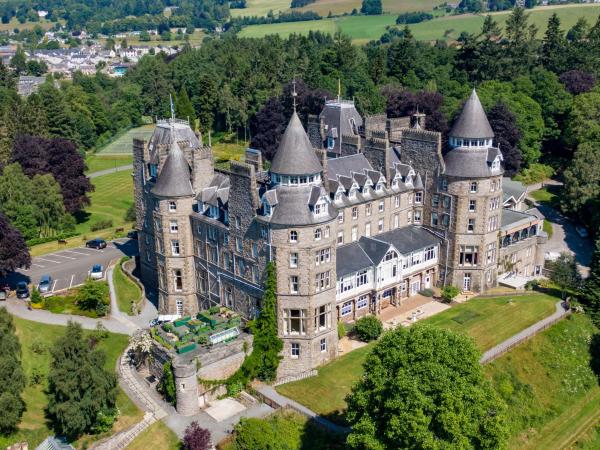 Large stone castle-like building with turrets surrounded by trees and green fields under daylight
