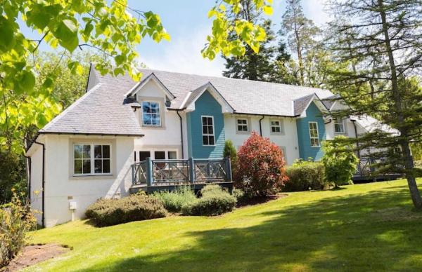White and blue lodge with small balconies surrounded by green trees and lawn on a sunny day