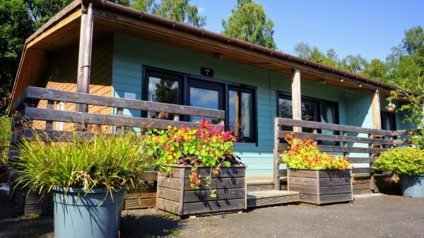Single-story wooden lodge with blue siding, black-framed windows, and flower boxes on the front porch
