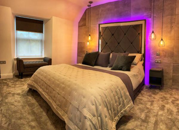 Double bed with tufted headboard, purple lighting, bedside lamps, window with blind, and bench seat in bedroom