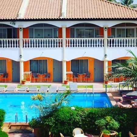 Two-story hotel building with orange and white walls, balconies, and a pool with lounge chairs in front
