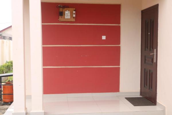 entrance area with a dark wooden door, red and cream wall, white tiled floor, and a small black mat