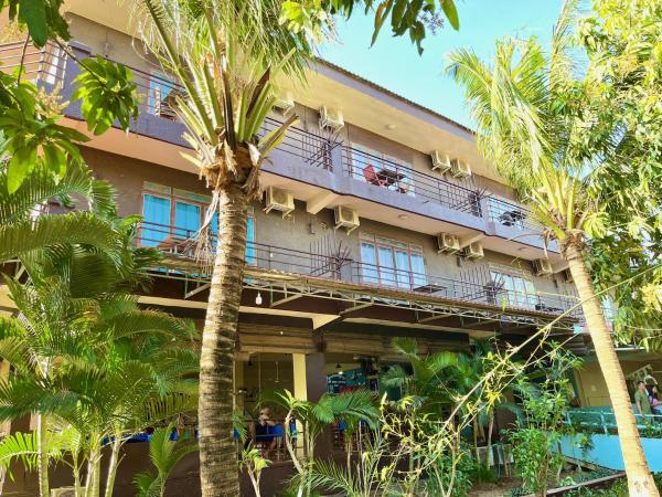 Three-story hotel building with balconies and air conditioners surrounded by palm trees and greenery under a clear sky
