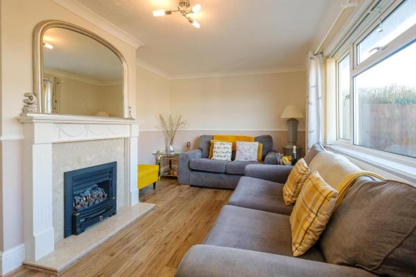 Living room with two grey sofas, yellow cushions, a fireplace with a large mirror, and a window with curtains