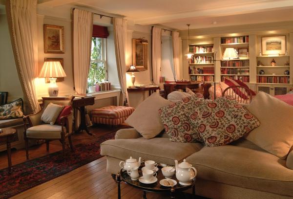 Cozy lounge with beige sofa, patterned cushions, wooden floor, bookshelves, and soft lighting from lamps