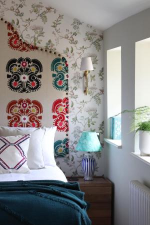 bed with white pillows and teal throw beside wooden nightstand with blue lamp under floral wallpaper