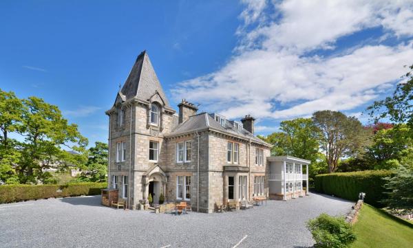 Stone hotel building with a tall turret under a blue sky surrounded by trees and gravel parking area