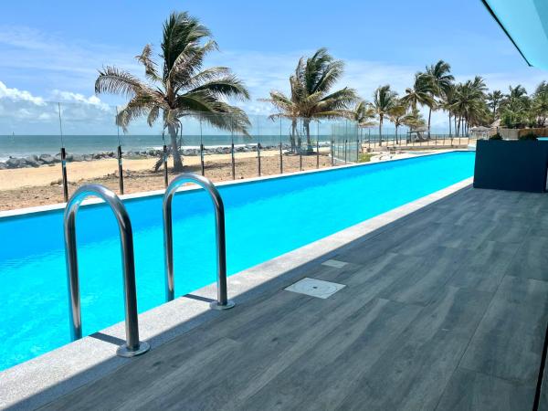 Long outdoor pool with metal ladder beside a tiled patio overlooking palm trees and sandy beach under blue sky
