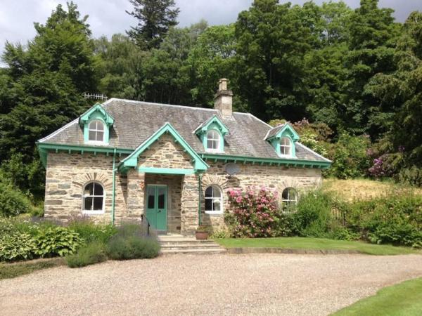 Stone cottage with green trim surrounded by trees and garden under a cloudy sky