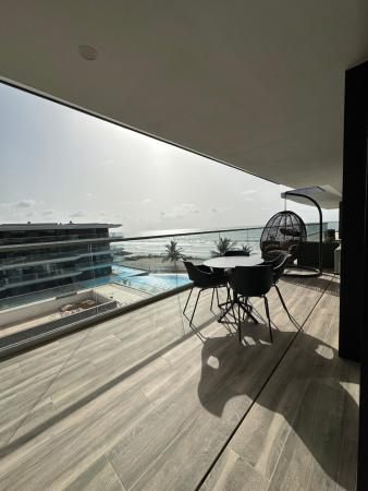 Balcony with round table, four chairs, and hanging chair overlooking pool, palm trees, and ocean in daylight