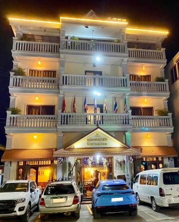 Four-story guesthouse building lit at night with parked cars in front and flags on the balcony