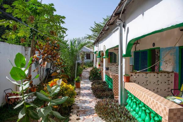 Outdoor walkway with plants and white building with green trim and small balconies at Happy Corner Lodge Janjangbureh