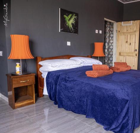 bed with blue blanket and orange towels in room with dark walls, wooden door, bedside table, and orange lampshades