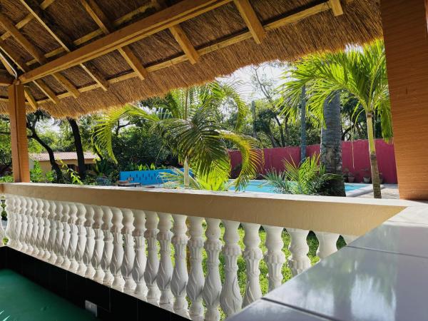 view from a thatched roof veranda showing white balustrade, palm trees, and a blue swimming pool