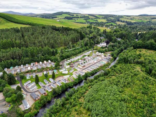 aerial view of a holiday park with rows of caravans beside a river and surrounded by green hills and forests