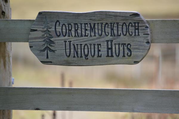 wooden sign with tree illustration reading Corriemuckloch Unique Huts on a wooden fence