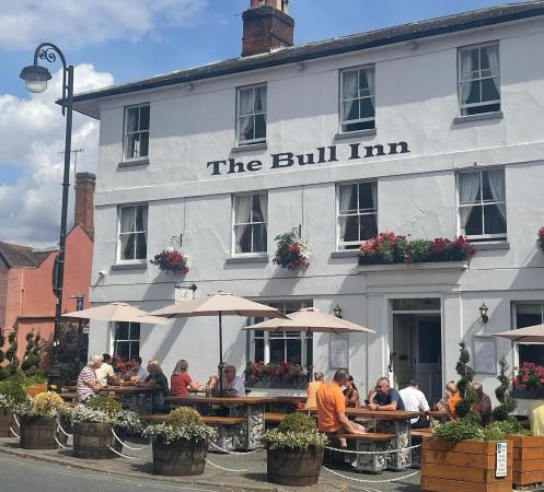 People sitting under umbrellas at outdoor tables outside The Bull Inn pub on a sunny day