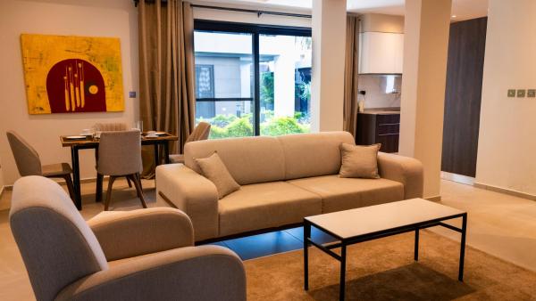 Living area with beige sofa, armchair, coffee table, dining table with four chairs, and large window with garden view