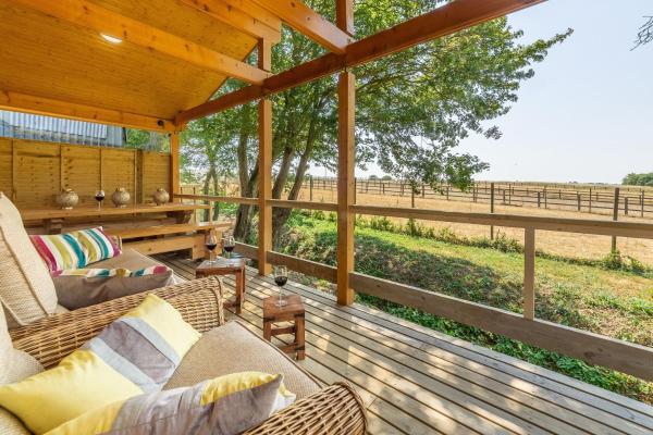 Covered wooden deck with cushioned wicker chairs, small tables with wine glasses, overlooking fenced fields and trees