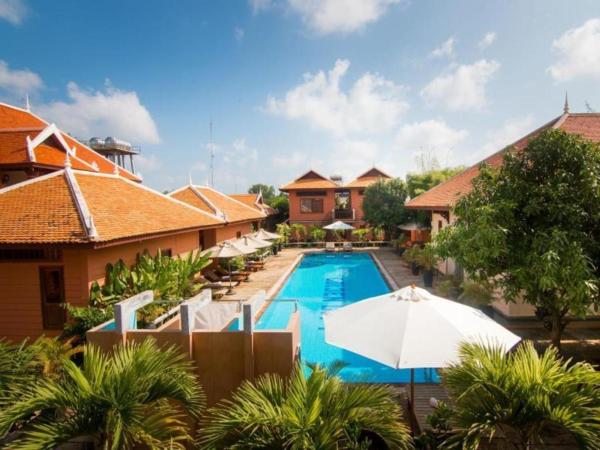 Outdoor swimming pool surrounded by buildings with orange tiled roofs and green plants under a blue sky