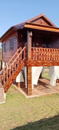 wooden elevated bungalow with stairs and carved railings under clear sky on grassy ground