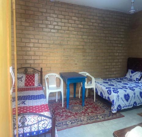 Room with two beds, a blue table, two white plastic chairs, and a patterned rug on tiled floor