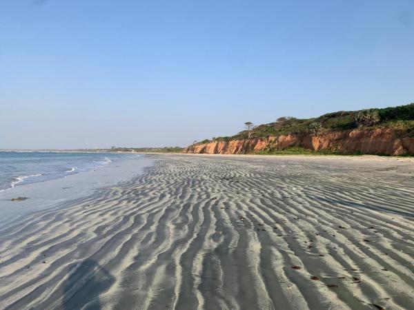 Rippling wet sand on a wide beach with low cliffs and sparse vegetation under a clear blue sky