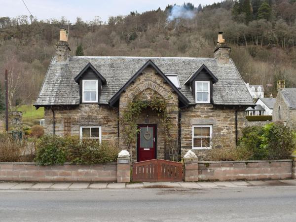 stone cottage with slate roof, two dormer windows, red door, and garden behind low stone wall