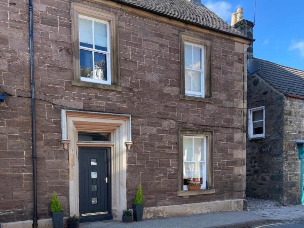 Stone house with dark door and four white-framed windows, two with curtains and one with flower pot