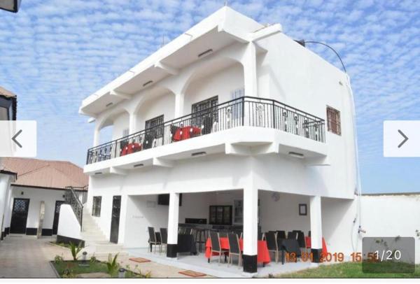 white two-story guest house with balcony and outdoor seating under a partly cloudy sky