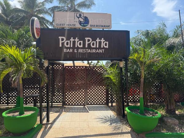Entrance to Patta Patta bar and restaurant with wooden lattice gate and green potted palm trees on a sunny day