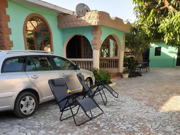 Two reclining chairs in front of a silver car parked by a turquoise bungalow with arched windows and a tiled courtyard