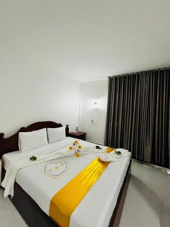 Two single beds with white linens and yellow runners in a simple hotel room with a nightstand and wall light