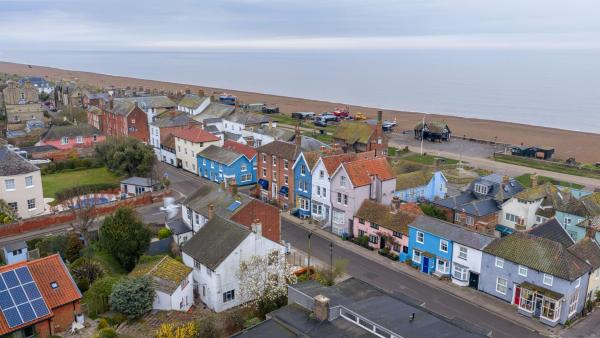 aerial view of a coastal village with colorful houses along a street near a pebble beach under a cloudy sky