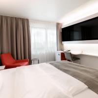 a hotel room with a large bed and a red chair at DORMERO Hotel Hannover