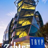 a tall glass building with a sign in front of it at TRYP by Wyndham Cuenca Zahir