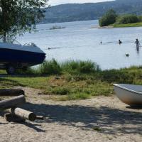 a boat on the shore of a lake with people in the water at Odin Camping AS, Svensrud