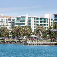 a large building with palm trees in front of a body of water at Novotel Geelong